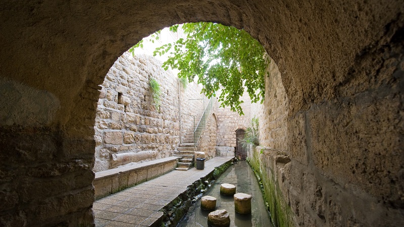 Siloamdammen i Jerusalem, en kanal med rester av fyra pelare, ovan ett stenvalv och i bakgrunden en stentrappa som leder upp till Davids stad.